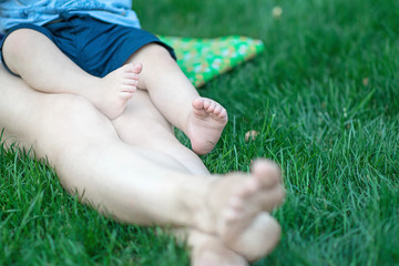 Baby feet on mother's legs relaxing on green grass at summer day