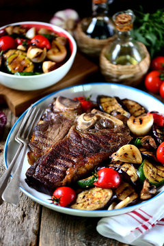 Grilled t-bone steak with grilled vegetables on an old wooden background. Rustic style.