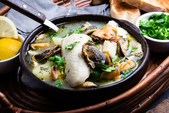 Seafood fish soup in clay bowls served with lemon and coriander. Closeup, copy space