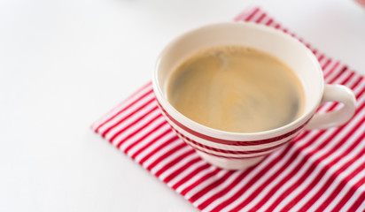 Red coffee cup over kitchen red strips towel. View from above. Isolated on white background