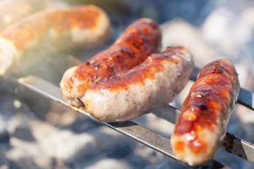 Close-up spicy sausages in smoke on the hot flat grill and skewers outdoors.