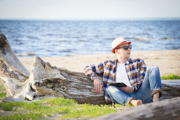 A man in smart casual hipster style with tablet combining work with relax on the beach of Baltic Sea
