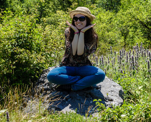 Smiling young girl with sunglasses and hat sitting on the rock