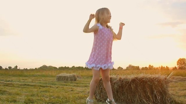 Happy little girl in a field with hay rolls at sunset