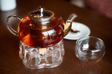 Glass infuser teapot with tea on the trivet and tea cup