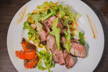 Roasted meat with blood in a cut with vegetables on a wooden background