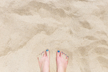 Young woman's foots with blue pedicure on the yellow sand