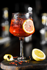 Red cold sangria lemonade cocktail with lemon and ice on dark background