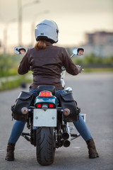 Rear view at the woman motorcyclist sitting on the classic chopper motorbike on urban asphalt road