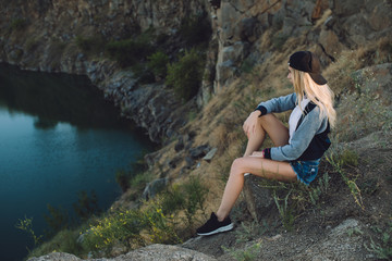 Naklejka premium Hiker girl. Trip alone. Young woman travel with adventure. She sitting on nature and looks to quarry.