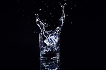 Isolated cold water in a glass with splash and cubes of ice on black background, brandy in a glass