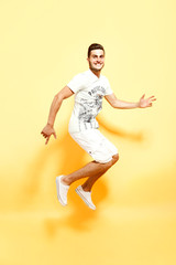 Fototapeta na wymiar Shot of handsome bearded guy dressed in white t-shirt and shorts jumping looking at camera smiling.