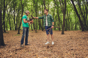 Two young male tourists in the wood in fall, collecting wood for a camp fire for barbeque, helping each other, team work