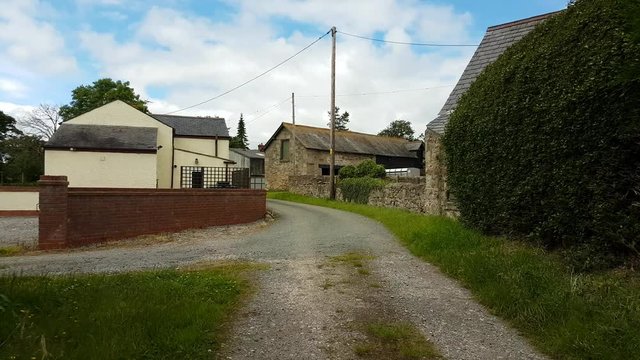 Footage walking down a green countryside lane in Mold, North Wales passing by farm buildings.