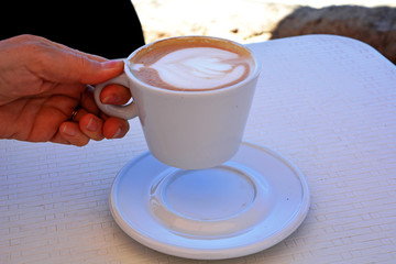 Delicious foamy cappuccino on a white cup on a plate.