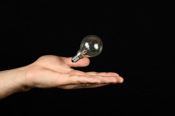 Male hand catches the incandescent bulb close isolated on black background. The concept of electricity and light