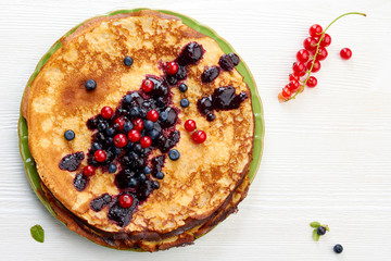 Thin pancakes with summer berries on white wooden table