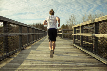 Male Jogger Running Outdoors. Young male runner in motion on wooden boardwalk outdoors.