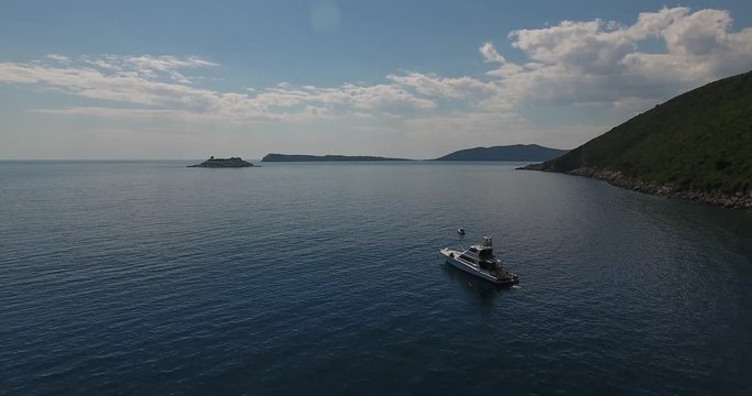 Beautiful panoramic view on the Lustica peninsula from the sea beach. Flying above Janica beach and boats, sailing in the sea. Summer on the Montenegro coast