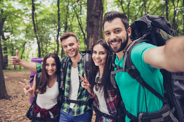 Close up of four cheerful  friends in the spring nice wood, embracing, posing for a selfie shot, that handsome brunet is taking
