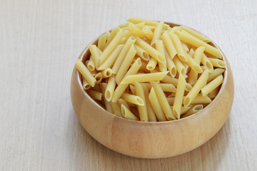 Raw Macaroni in the wooden bowl on wood background.