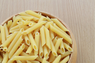 Raw Macaroni in the wooden bowl on wood background.