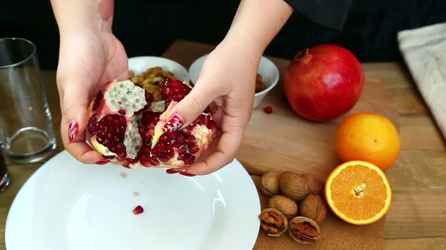 On a wooden table, a woman breaks a pomegranate by her own hands,. Hd shot with dolly .The camera moves from right to left.