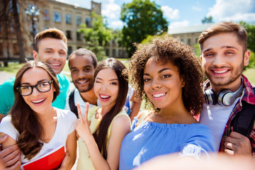 Selfie time! Six international students with beaming smiles are posing for selfie shot, african...
