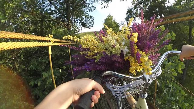 Slown motion. A girl on a bicycle with a bouquet of multicolored wildflowers in the corms before the wheel passes over a suspension bridge. Action camera go pro.