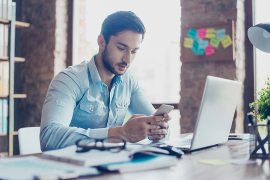 Close up of confident handsome young middle eastern lawyer guy is browsing information on his samrt phone at work place