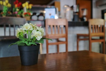 A plastic pot of bouquet flower on the wooden table in the restaurant. Vintage style.