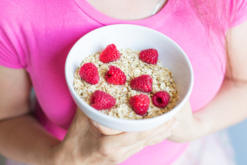 Woman's hands hold healthy and natural breakfast, oatmeal and raspberries in a bowl