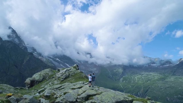 wanderlust moving backward over two people looking at mountain valley in sunny summer with clouds.Europe Alps outdoor green nature scape mountains wild aerial establisher.4k drone flight establishing