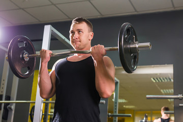 Fototapeta na wymiar Strong and handsome man lifting weights a barbell in a gym