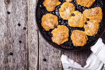 Homemade Blueberry cobbler in a cast iron skillet pan on a rustic wooden table. Organic natural food. Healthy breakfast. Top view. Selective focus 