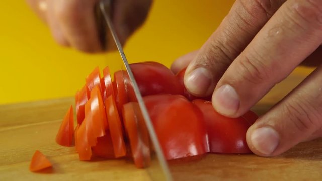 Male hands cutting red pepper on the wooden board against yellow background, shot in 4K, HD video