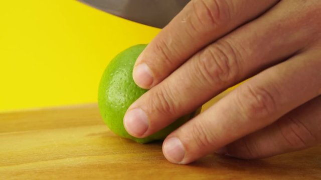 Man's hands cutting lime into four halves. Close up, yellow background.