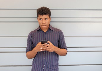 Young attractive man holding cell phone while standing alone and biting lip