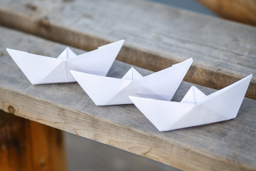Three white paper boats on wooden bench