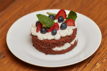 Chocolate cake with cream and berries on white plate