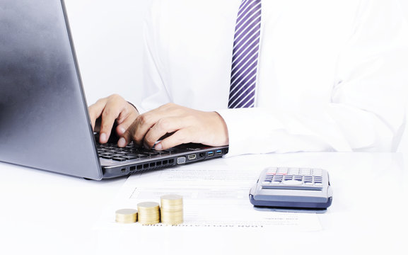 Business man typing laptop with calculator and coins stack on office desk for finance ideas concept