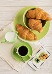 Coffee with milk, croissants and smart phone with photo.