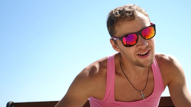Handsome fashionable guy with sunglasses in a pink T-shirt looks at the camera and suddenly points at camera