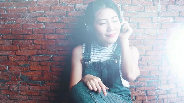 asian beautiful girl enjoy happiness moment with music and headphone near brown brick wall dolly shot