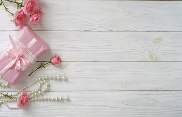 Bouquet of beautiful pink roses and gift in pink packing on white wooden background.Top view.Copy space
