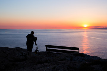 Fototapeta premium man photographer taking photos of sunset at the sea