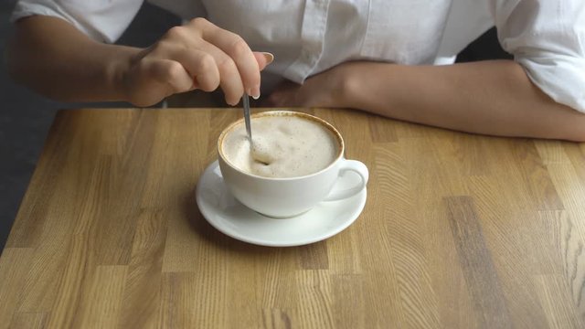 a young beautiful woman drinking coffee in a cafe. Hand of girl stiring sugar in coffee close up