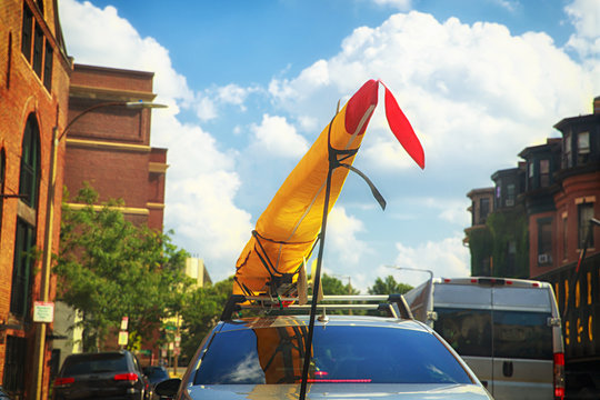 Kayak on the top of the car. Kayak in a yellow case is attached to the car. Urban background