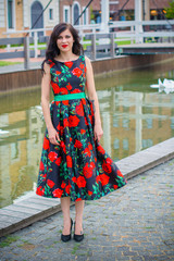 Gorgeous vintage brunette woman with curly hair on a style 50s in black dress with red roses. Pretty girl walk on a streets and have a good mood feeling wonderful