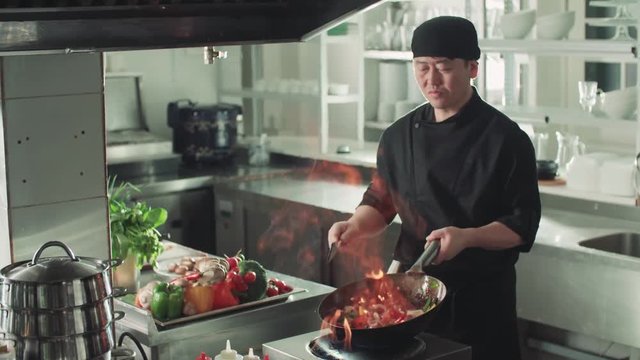 Asian chef works coloured mixed roasting vegetables in the wok with flame , kitchen Asian restaurant, slow motion